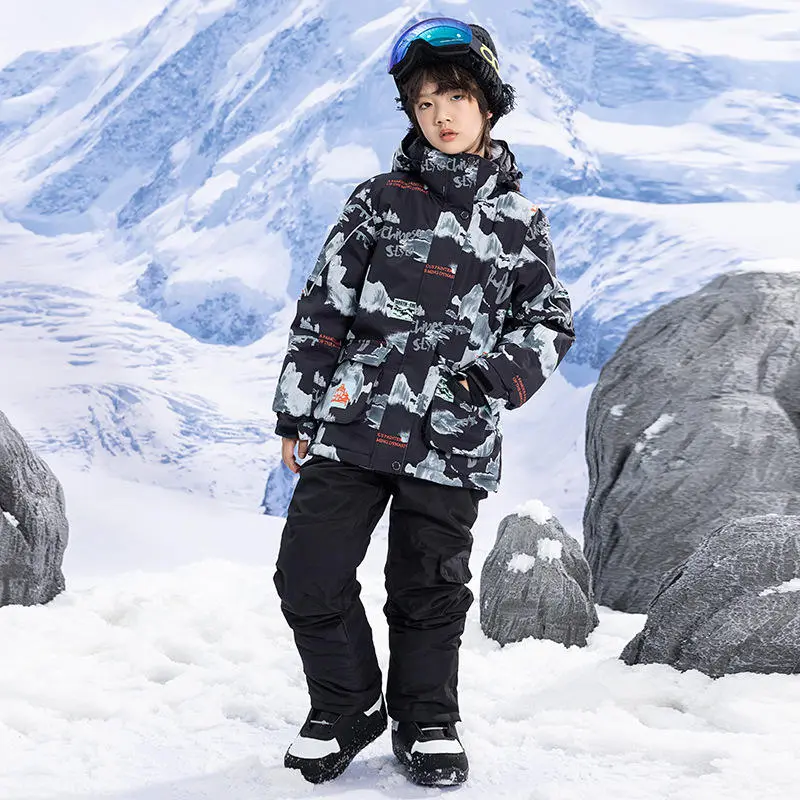 Boy wearing the kids' printed ski jacket in the dark ink-wash print with black ski pants, standing in the snow