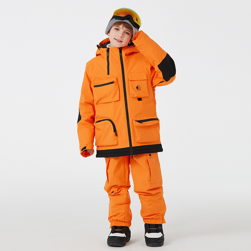 Boy wearing the orange two-piece ski set with black panels and cargo pockets, adjusting his goggles