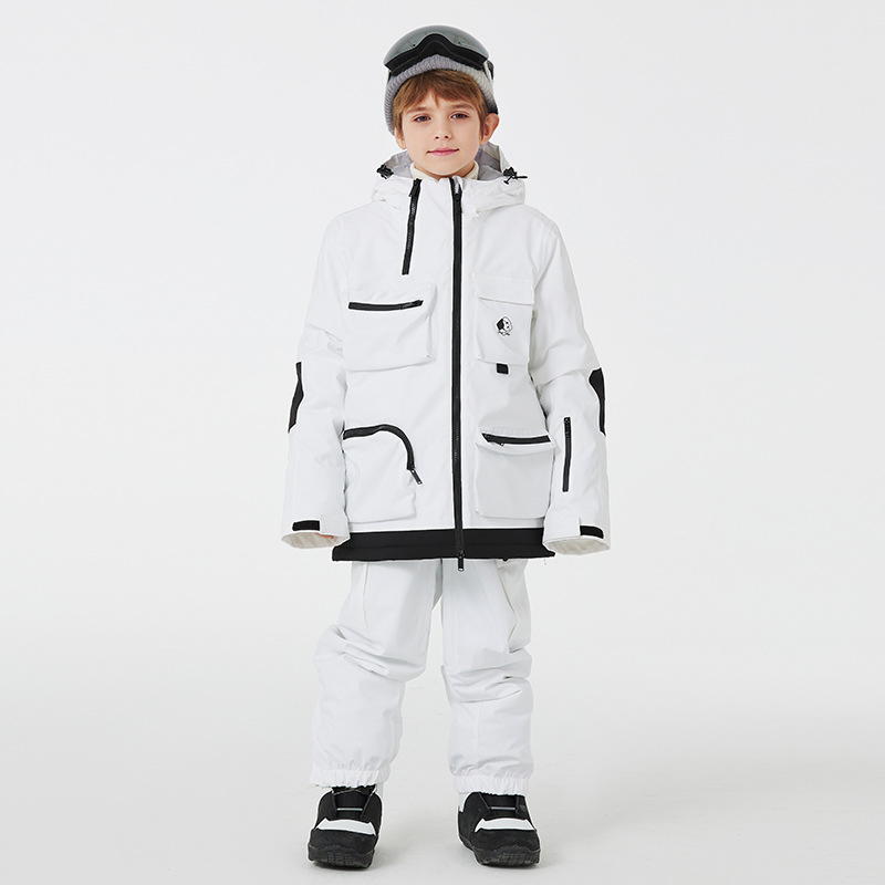 Boy wearing the white two-piece ski set with black trim and cargo pockets, front view